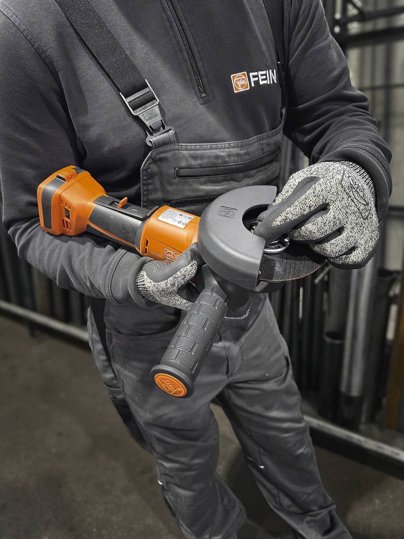 Een persoon in werkkleding monteert een slijpschijf op een haakse slijper en toont correct gereedschapsgebruik in een werkplaats.