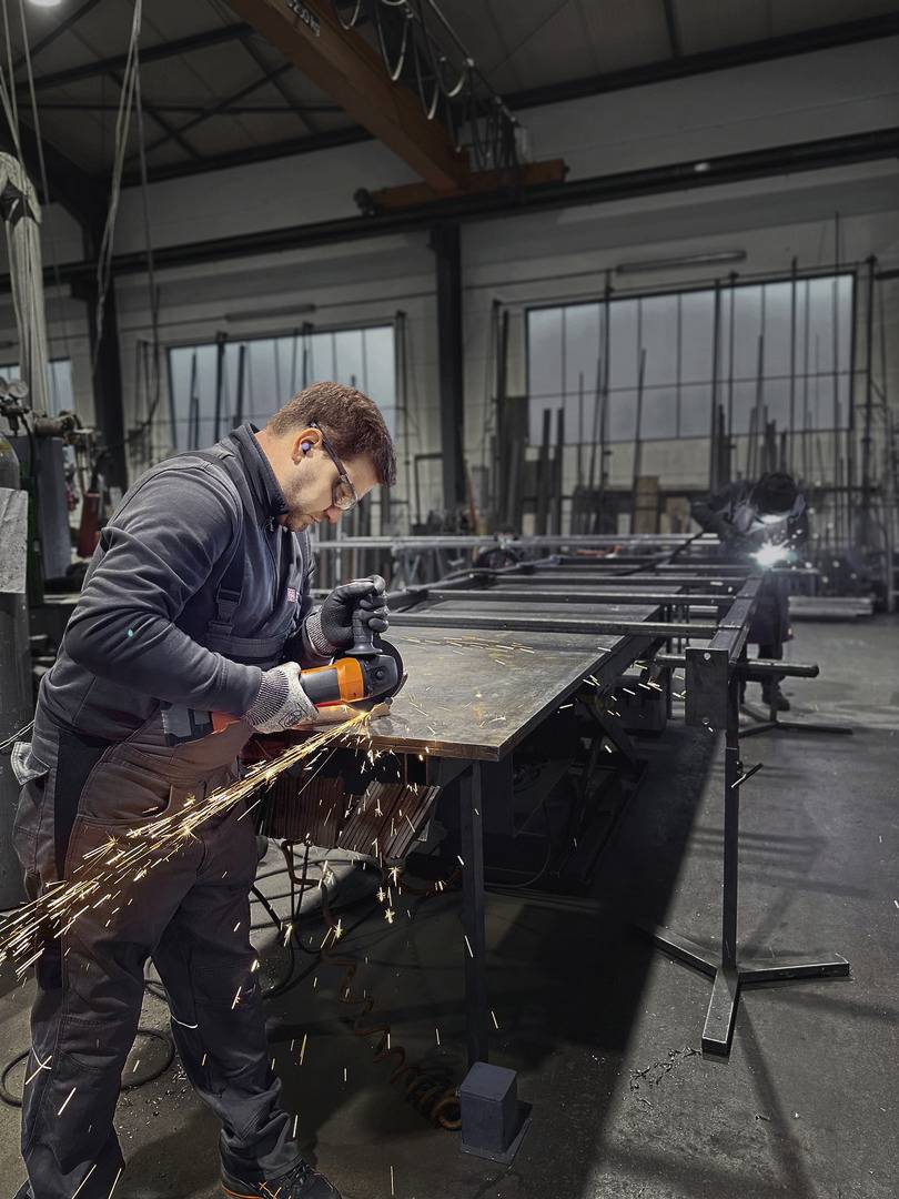 Een arbeider in beschermende uitrusting slijpt metaal in een werkplaats, vonken spatten van de slijpmachine.