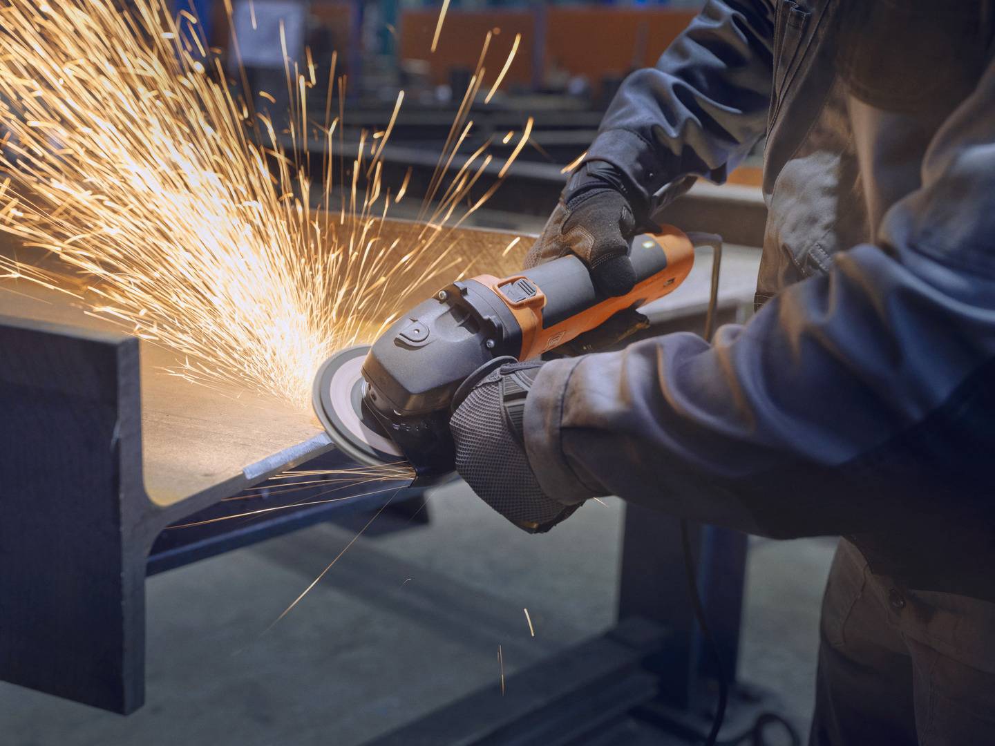 Een persoon slijpt metaal met een haakse slijper, vonken spatten rond. Werkt in een werkplaats of fabriek.