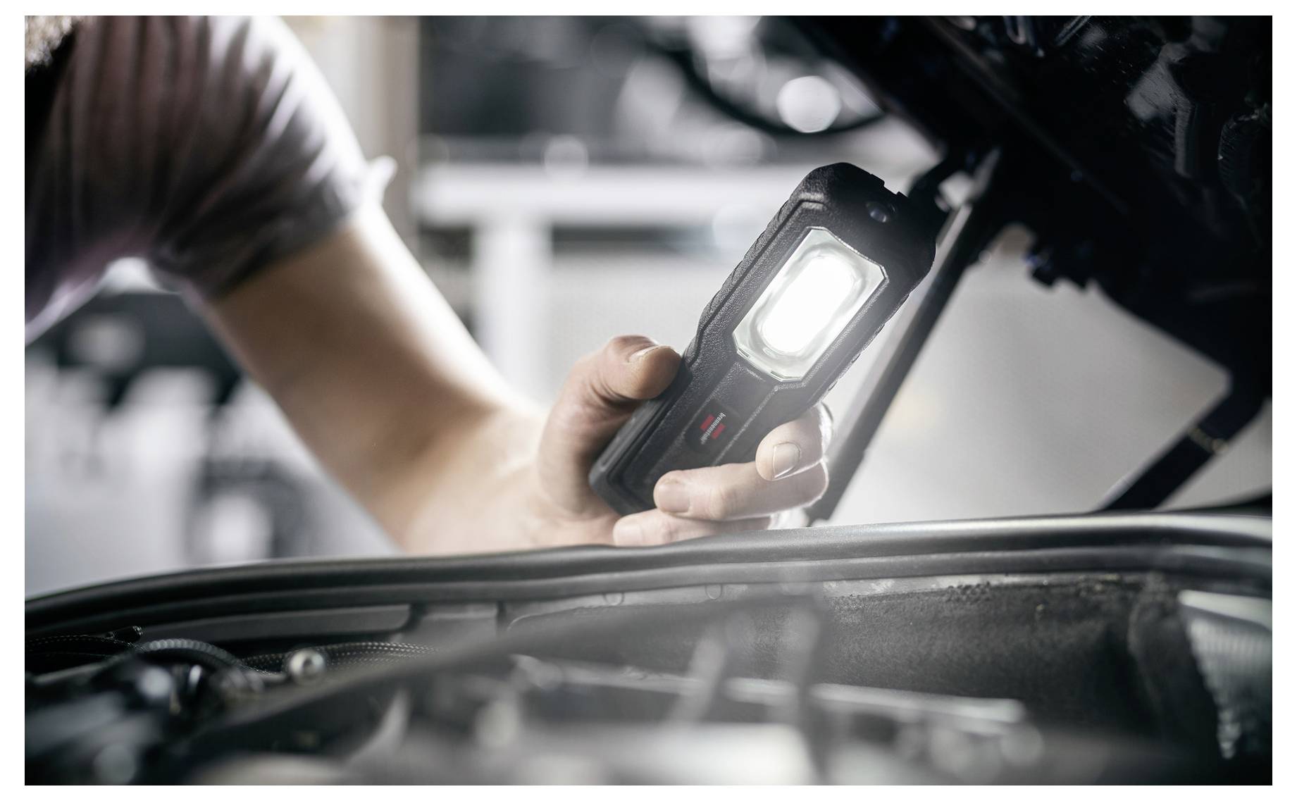 Monteur die een draagbare inspectielamp gebruikt om een motorcompartiment van een auto van dichtbij te onderzoeken.