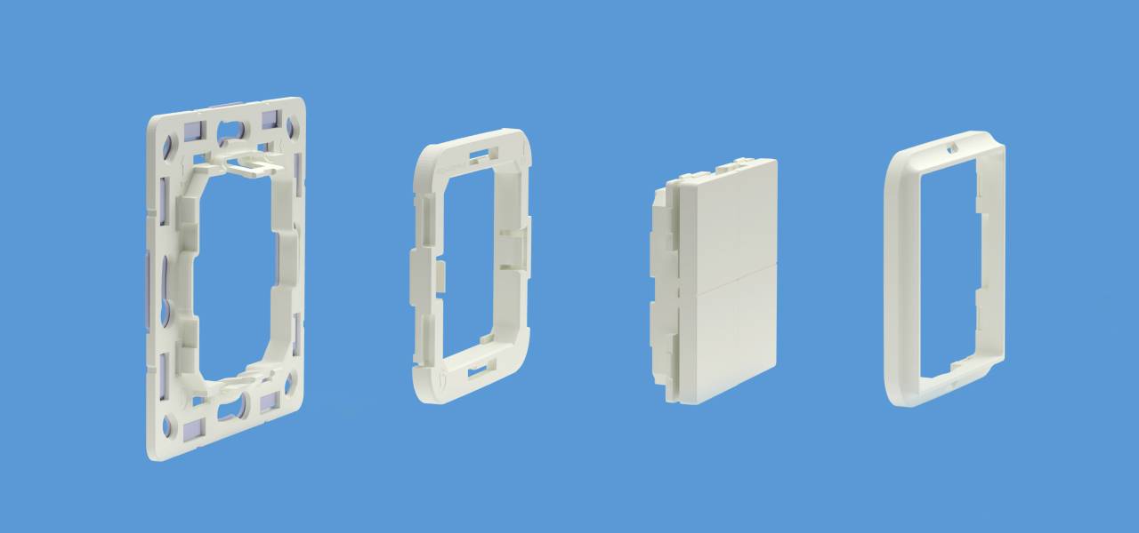 Vier kunststof onderdelen op een blauwe achtergrond die stapsgewijs een wandcontactdoos of een schakelaarframe vormen.