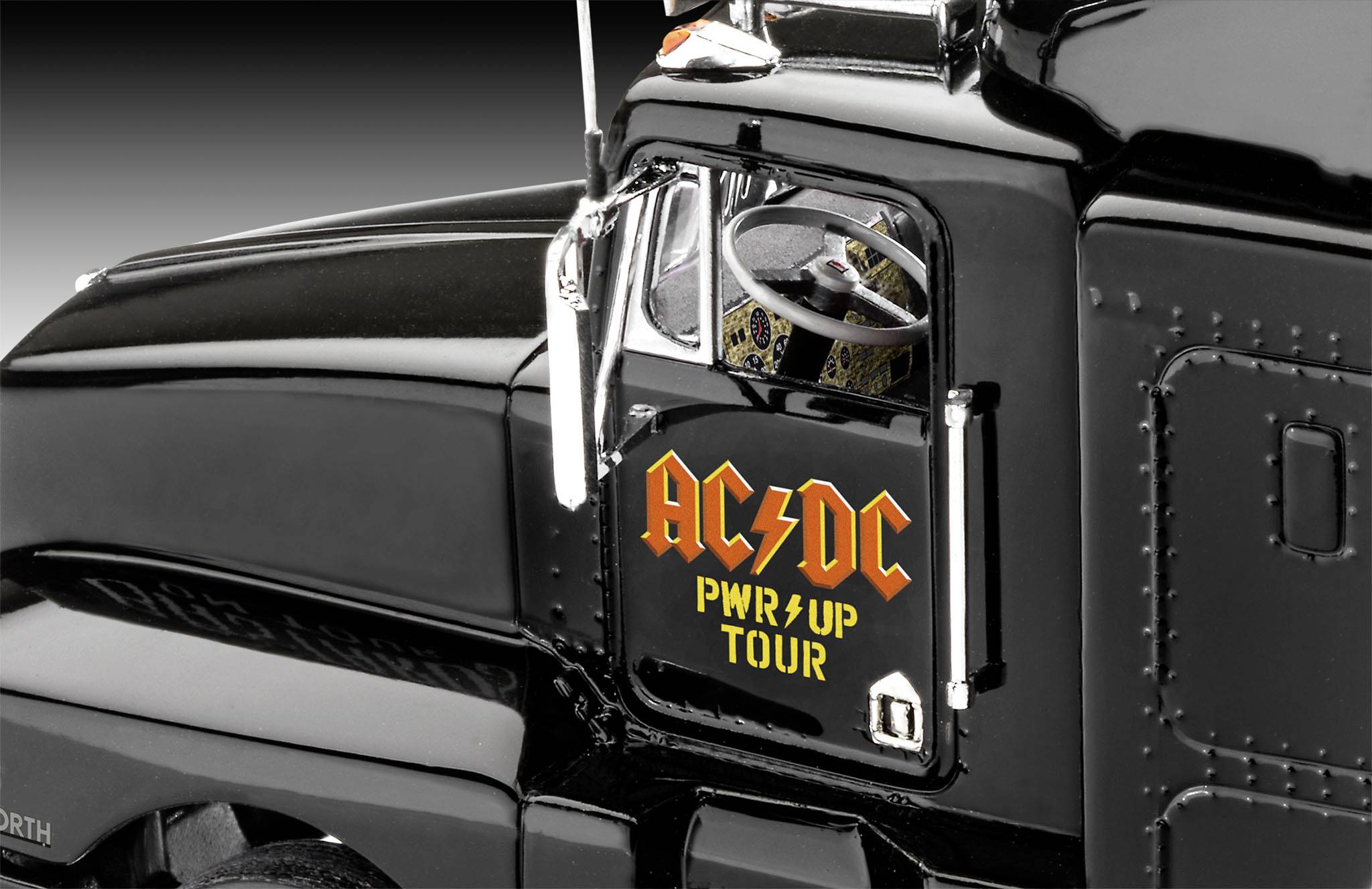 Zwarte vrachtwagen met 'AC/DC PWR/UP TOUR' op de zijdeur, gedetailleerde binnenkant zichtbaar. Luchtfoto toont glanzend oppervlak.