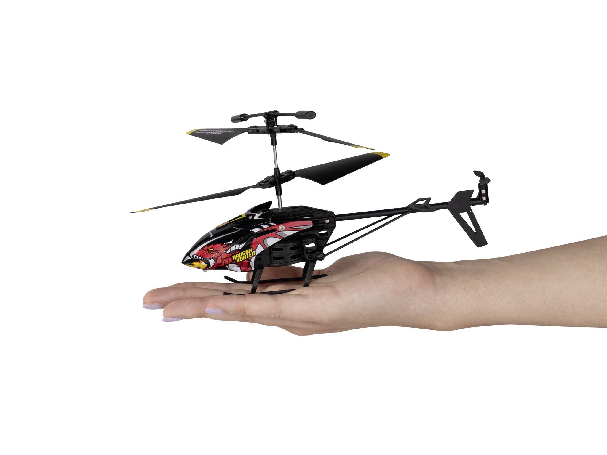 Een hand houdt een kleine afstandbestuurde helikopter vast met draaiende rotorbladen. De helikopter is zwart en rood.