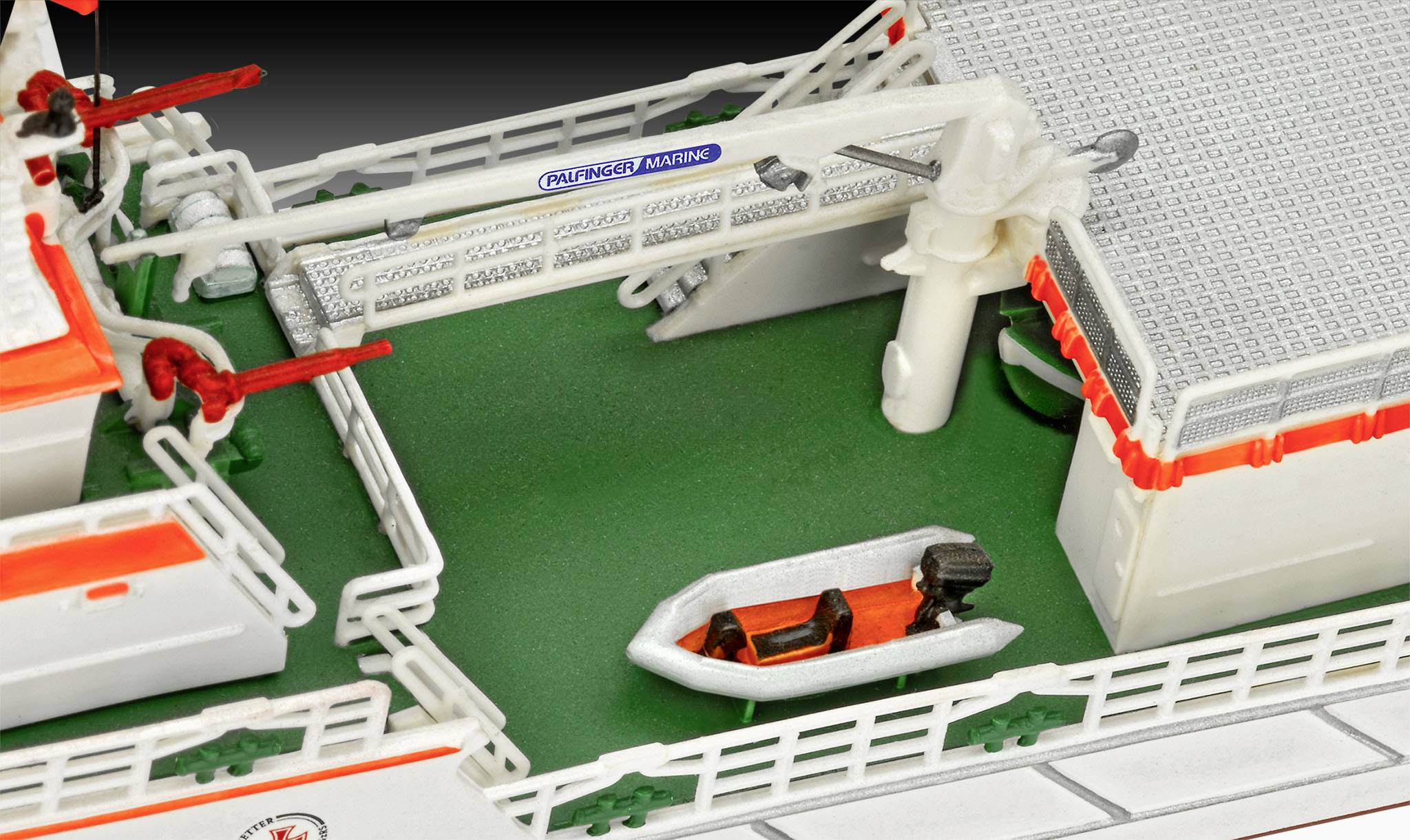 Model van een scheepsdek met een oranje-grijze rubberboot en details zoals lieren en reling in beeld.