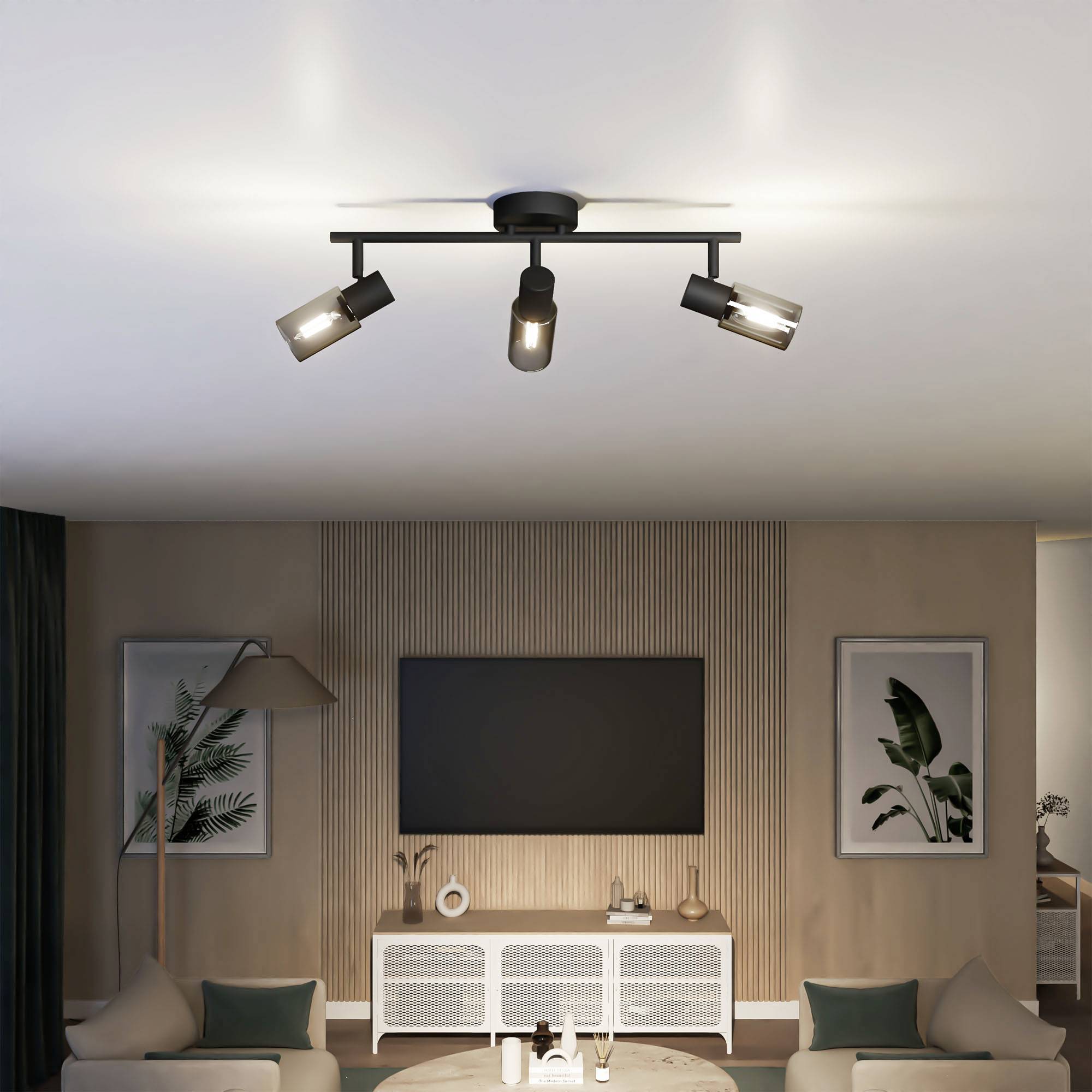 Woonkamer met moderne plafondverlichting, een flatscreen tv aan een houten lamellenwand, een grijs bankstel en planten in een modern design.