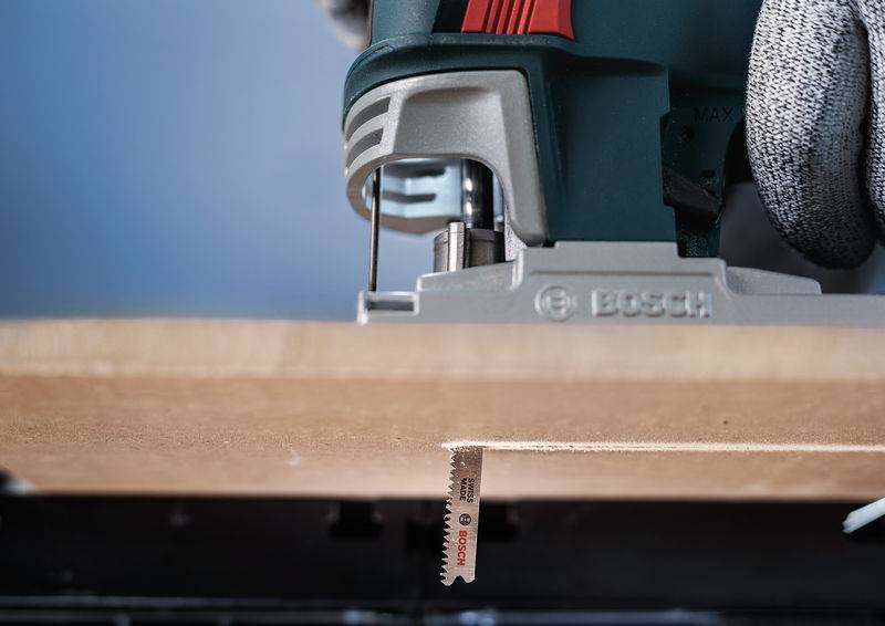 Een decoupeerzaag snijdt precies door een houten plank. Een handschoen houdt het apparaat stevig vast.