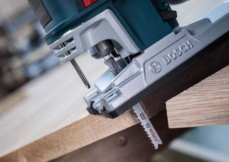 Een elektrische decoupeerzaag van Bosch zaagt door een houten plank. Close-up toont de zaagbeweging en het scherpe zaagblad.