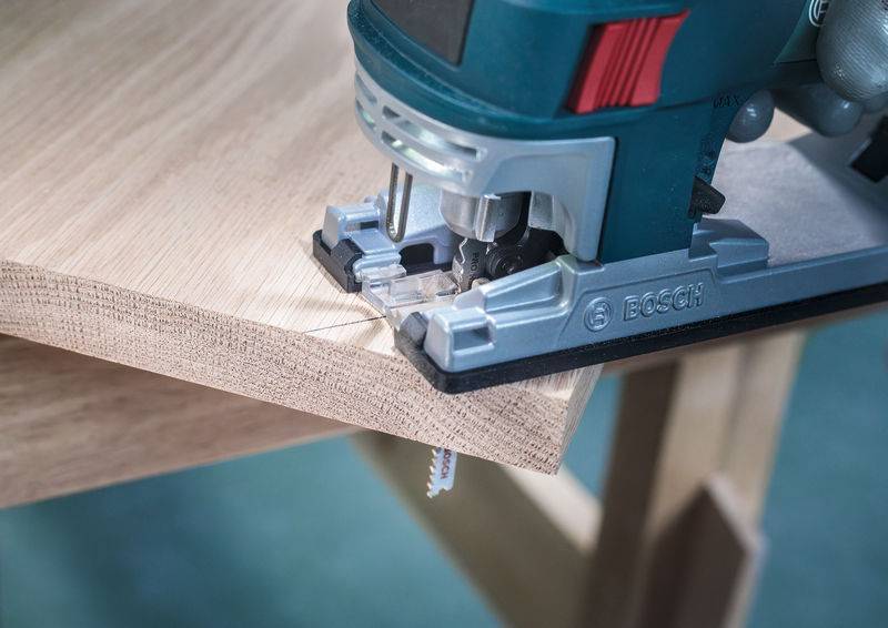 Een decoupeerzaag zaagt hout langs een geleidingslijn. Houtspaanders zijn zichtbaar terwijl de zaag door het materiaal werkt.