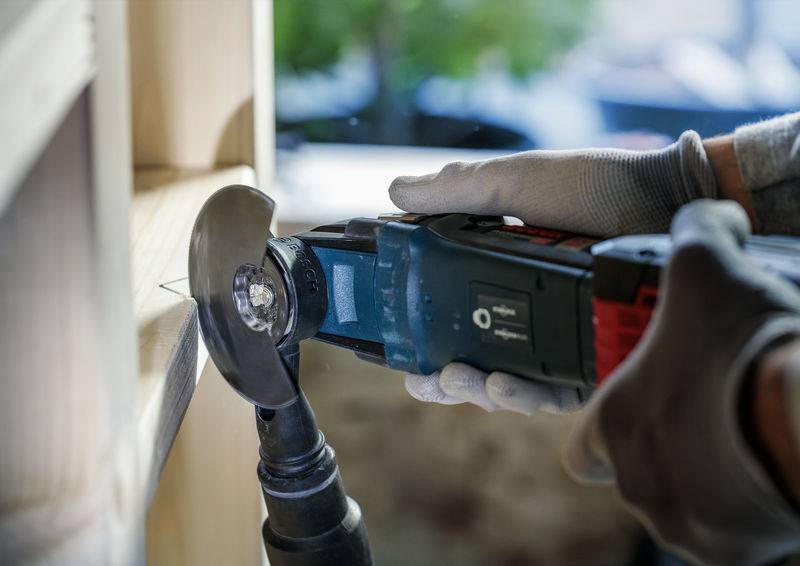 Een persoon werkt met een elektrische slijpmachine aan een houten frame. Ze draagt werkhandschoenen.
