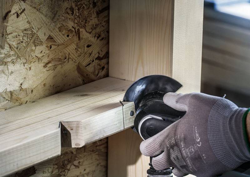 Ambachtsman slijpt hout met haakse slijper. Veiligheidsbril en handschoenen gedragen voor bescherming. Gedetailleerde close-up van de werkplek.