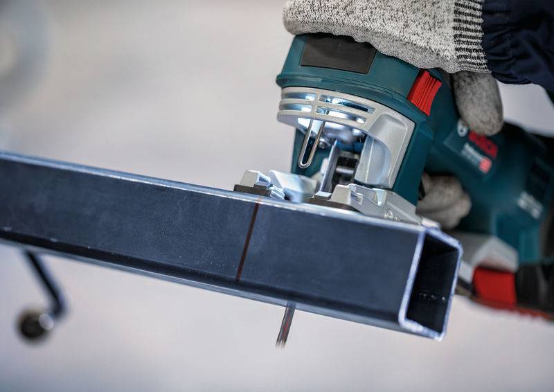 Een persoon zaagt een metalen buis door met een elektrische zaag. De hand draagt een werkhandschoen om veiligheid te waarborgen.