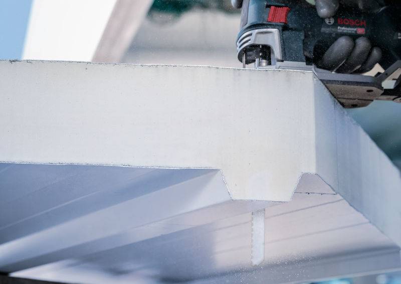 Een close-up van een elektrisch gereedschap dat een nauwkeurige sleuf in een witte kunststofplaat zaagt, vermoedelijk voor bouw- of vakmanswerkzaamheden.