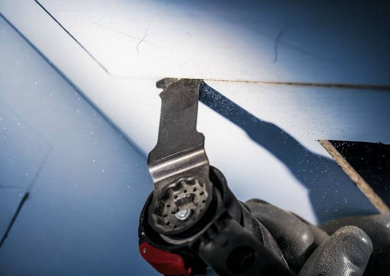 Een close-up van een elektrische zaag die een stuk materiaal doorsnijdt. De grijze handschoenen van de gebruiker zijn gedeeltelijk zichtbaar.