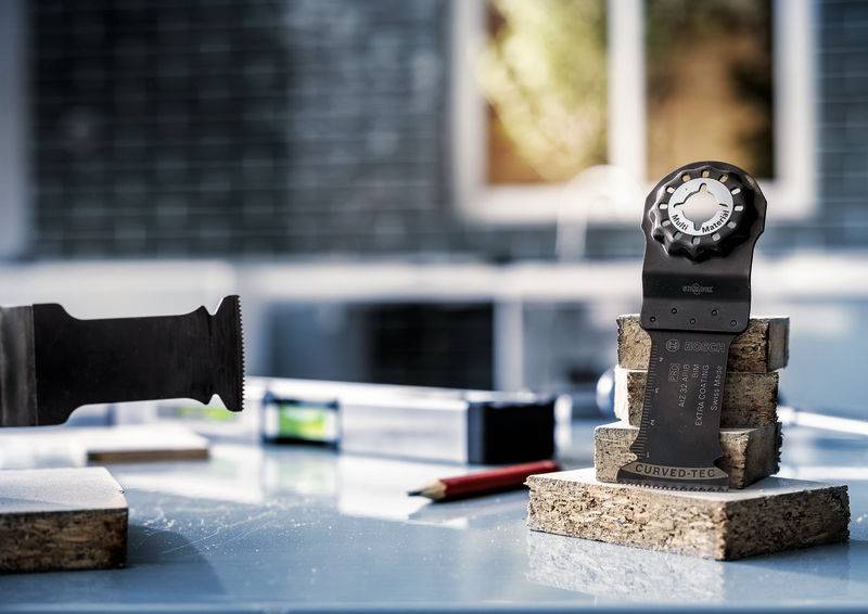 Close-up van een gereedschap met zaagbladen op een tafel met houten blokken op de achtergrond van een werkplaats met ramen.