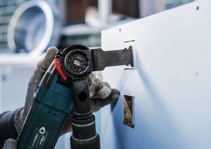 Een persoon maakt met een elektrisch gereedschap een rechthoekig gat in een muur. Close-up van het gereedschap tijdens het snijproces.