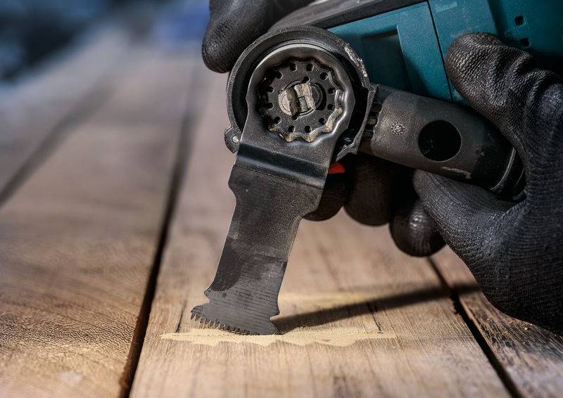 Een persoon werkt met een elektrisch multifunctioneel gereedschap en snijdt nauwkeurig een verdieping uit in een houten plank.