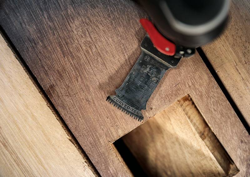 Close-up van een stuk hout met een uitsnijding. Een elektrisch zaagblad is zichtbaar aan de rand.