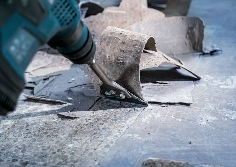 Een elektrisch gereedschap verwijdert tegelresten van een vloer. De boor verwijdert brokkelig materiaal en vuil op een bouwplaats.
