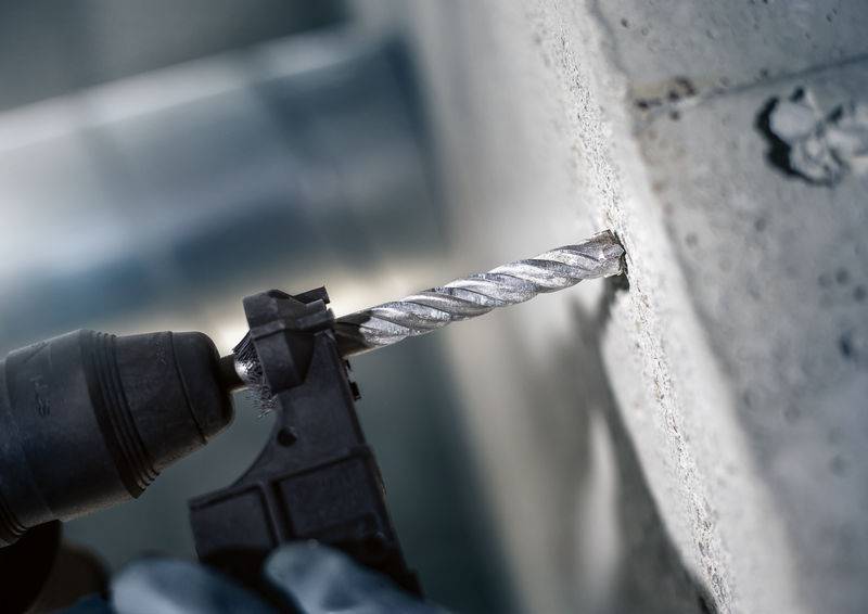 Een elektrische boormachine boort een gat in een betonwand. De boor is spiraalvormig en dringt door in het materiaal.
