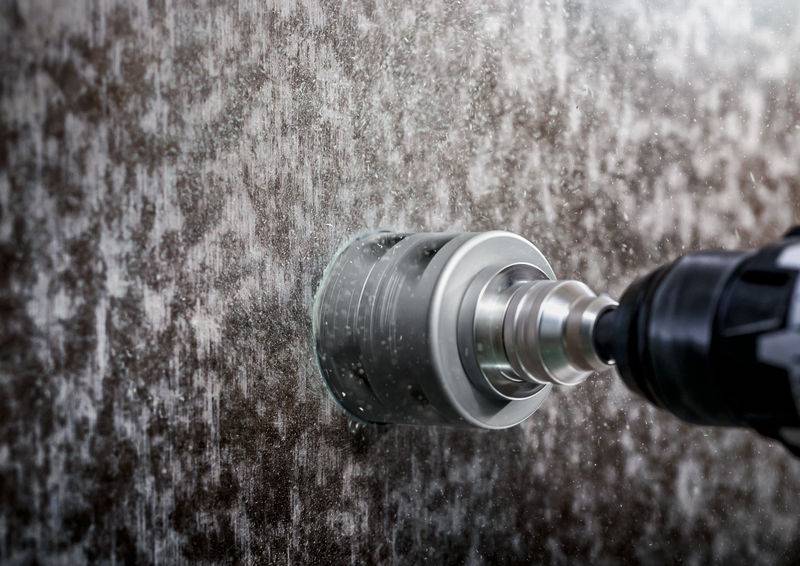 Een boor boort door een natte, donkere steenoppervlakte, waarbij water zichtbaar op de steen spat.