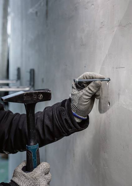 'Hand in werkhandschoen houdt hamer en beitel vast om in betonnen muur te beitelen.'