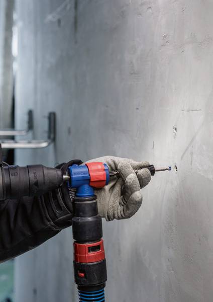 Een persoon met handschoenen houdt een boormachine tegen een muur en boort een gat in het beton.