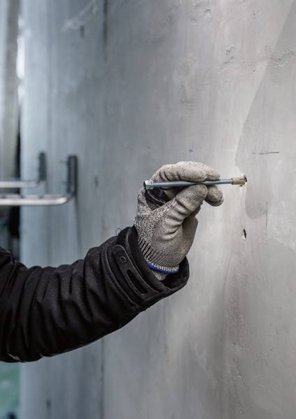 Een persoon met grijze handschoenen en een zwarte jas tekent met een pen op een grijze muur.