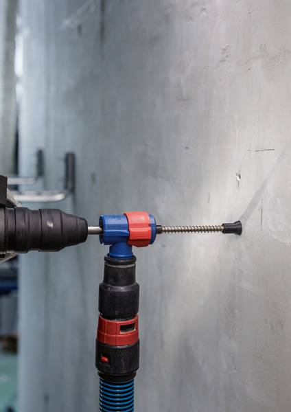Een boormachine wordt gebruikt om een gat in een grijze muur te boren. Een stofzuiger is gemonteerd bij de boorlocatie.
