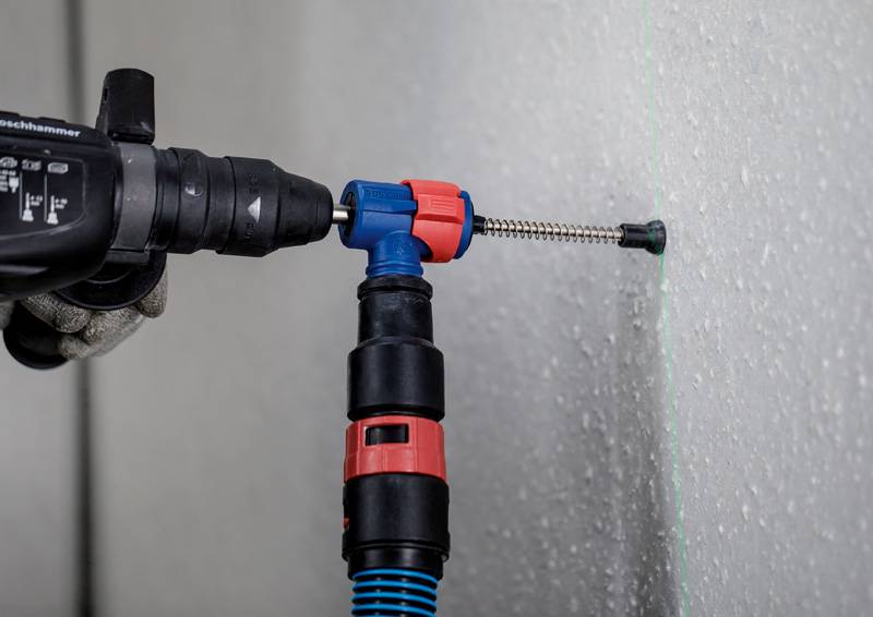 'Een arbeider gebruikt een boorhamer om een schroef in een muur te bevestigen. Een groene laserwaterpas is zichtbaar op de muur.'