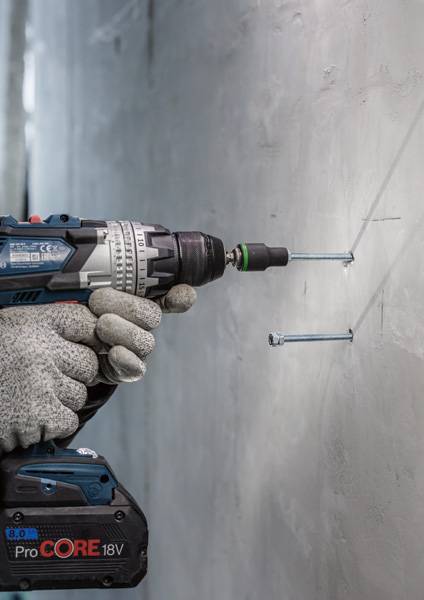 Een hand houdt een accuboormachine vast en bevestigt schroeven in een betonnen muur.