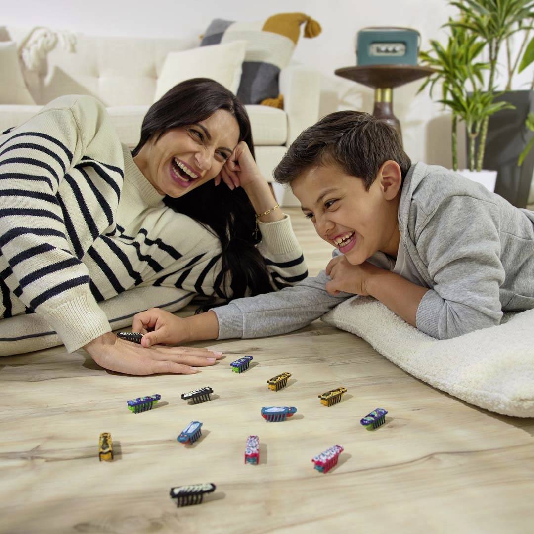 Een lachende vrouw en een jongen spelen samen op de vloer met kleine auto's in een woonkamer.