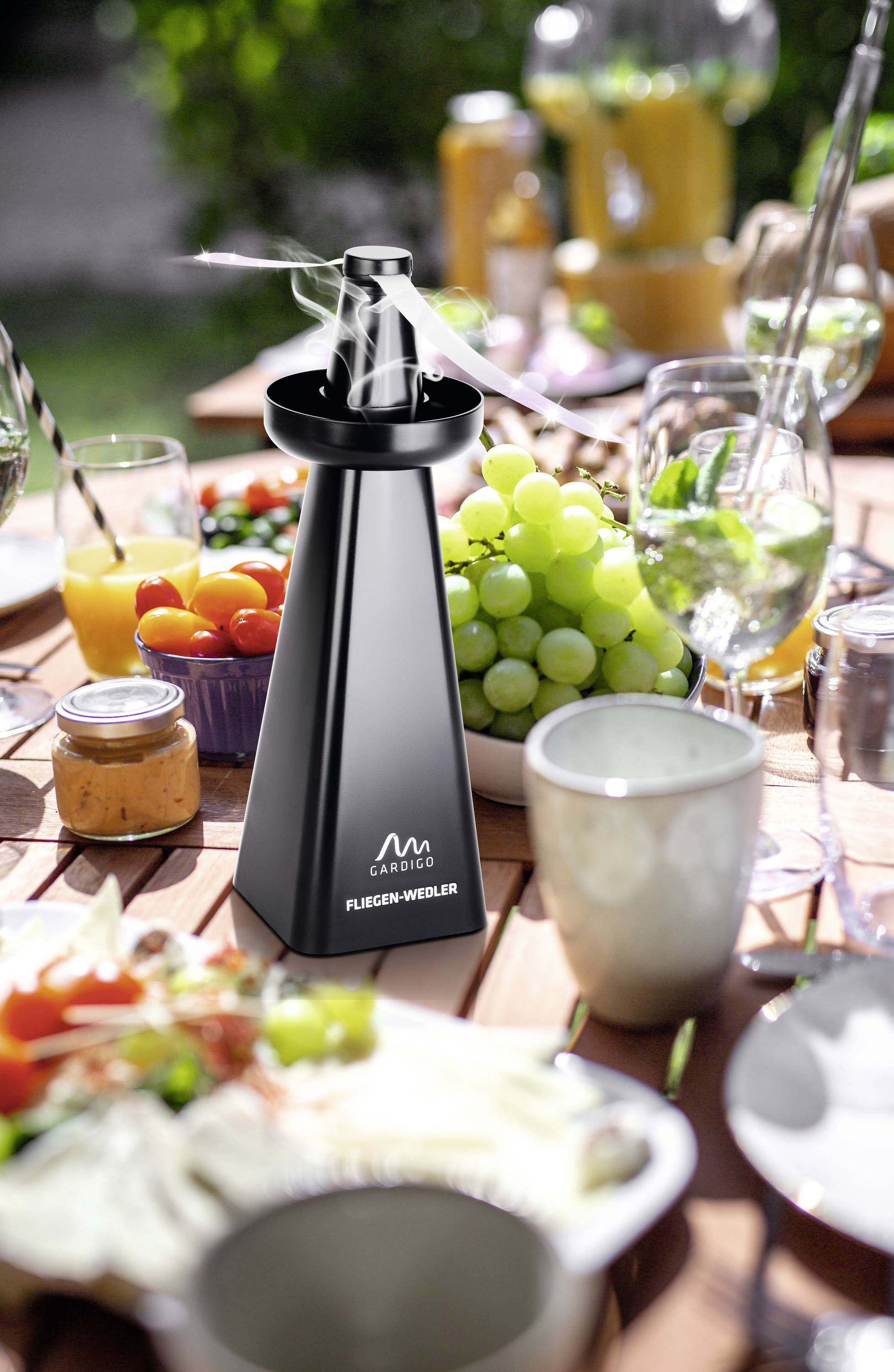 Zwarte elektronische pepermolen op een gedekte tuintafel met gerechten en dranken. Op de achtergrond vers fruit en sap.