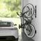 Een auto staat in een garage naast twee verticaal aan de muur bevestigde fietsen. Op de achtergrond is een groene ruimte zichtbaar.