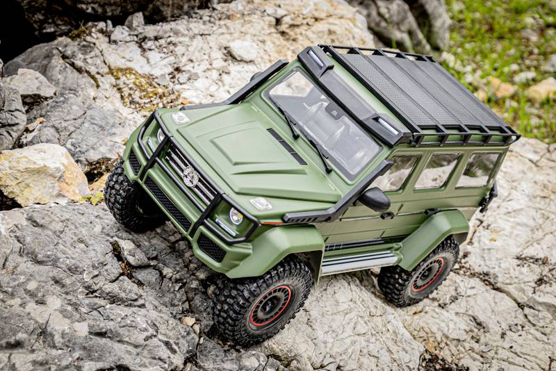 RC-modelauto in robuust, terreinvaardig ontwerp, rijdt over rotsachtig terrein. Voertuig is uitgevoerd in legergroen met dakdragers.