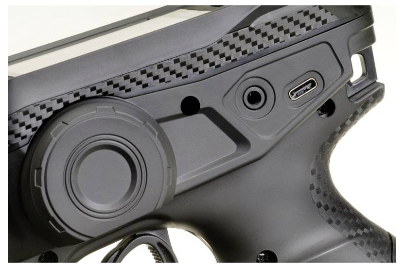 Close-up van een zwart elektronisch apparaat met een grote ronde knop en meerdere aansluitingen.