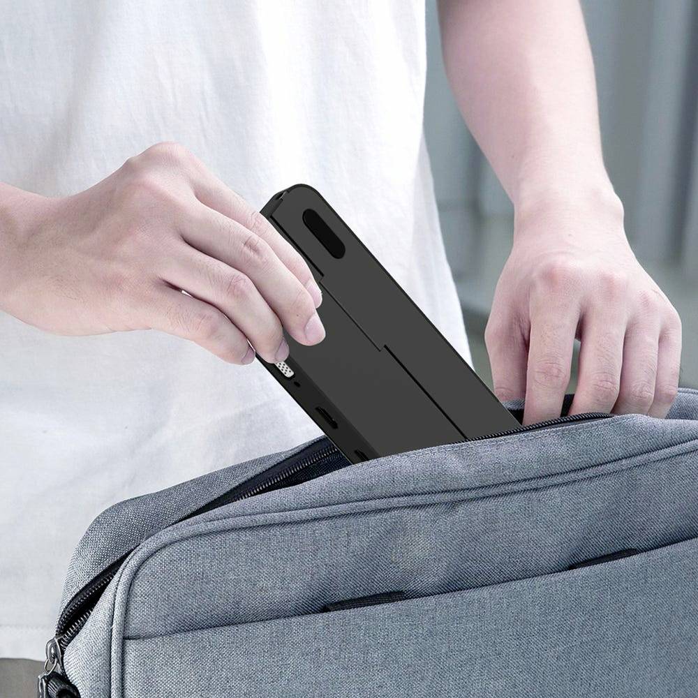Een persoon steekt voorzichtig een smartphone in een grijze, open tas.
