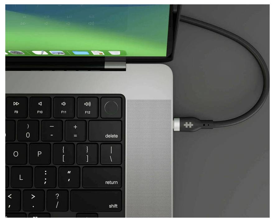 Een laptop met een aangesloten oplaadkabel. Het scherm toont een groene achtergrond. Toetsenbord zichtbaar, focus op de oplaadaansluiting.
