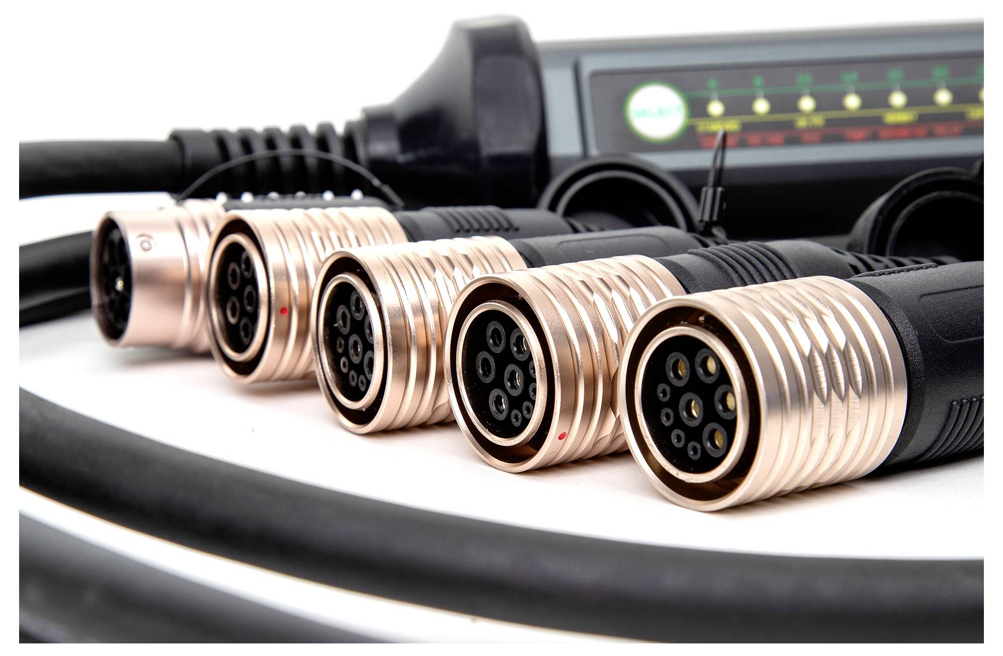 Verschillende ronde stekkers met koperen behuizing liggen op een rij voor een elektronisch apparaat met controlelampjes op de achtergrond.
