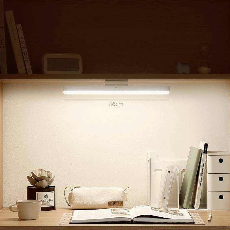 Een bureau met een ingeschakelde LED-lamp boven boeken en schrijfmateriaal. De verlichting creëert een warme, gezellige sfeer.