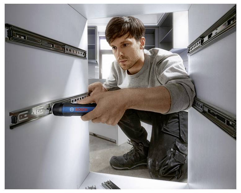 Een vakman installeert een ladegeleiding met een blauw elektrisch gereedschap in een lichte, moderne keuken.