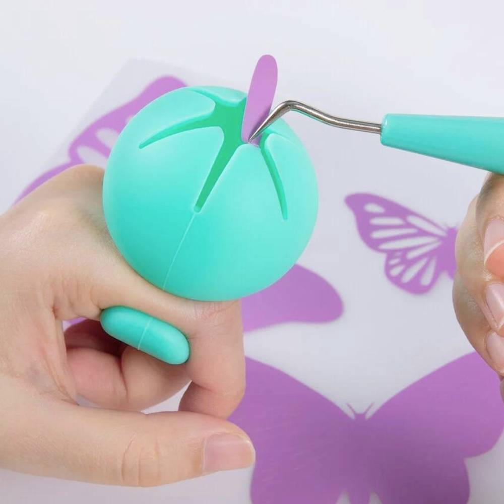 Twee handen houden een turquoise gereedschap vast dat een paarse tong uitsteekt. Op de achtergrond zijn vlindermotieven zichtbaar.