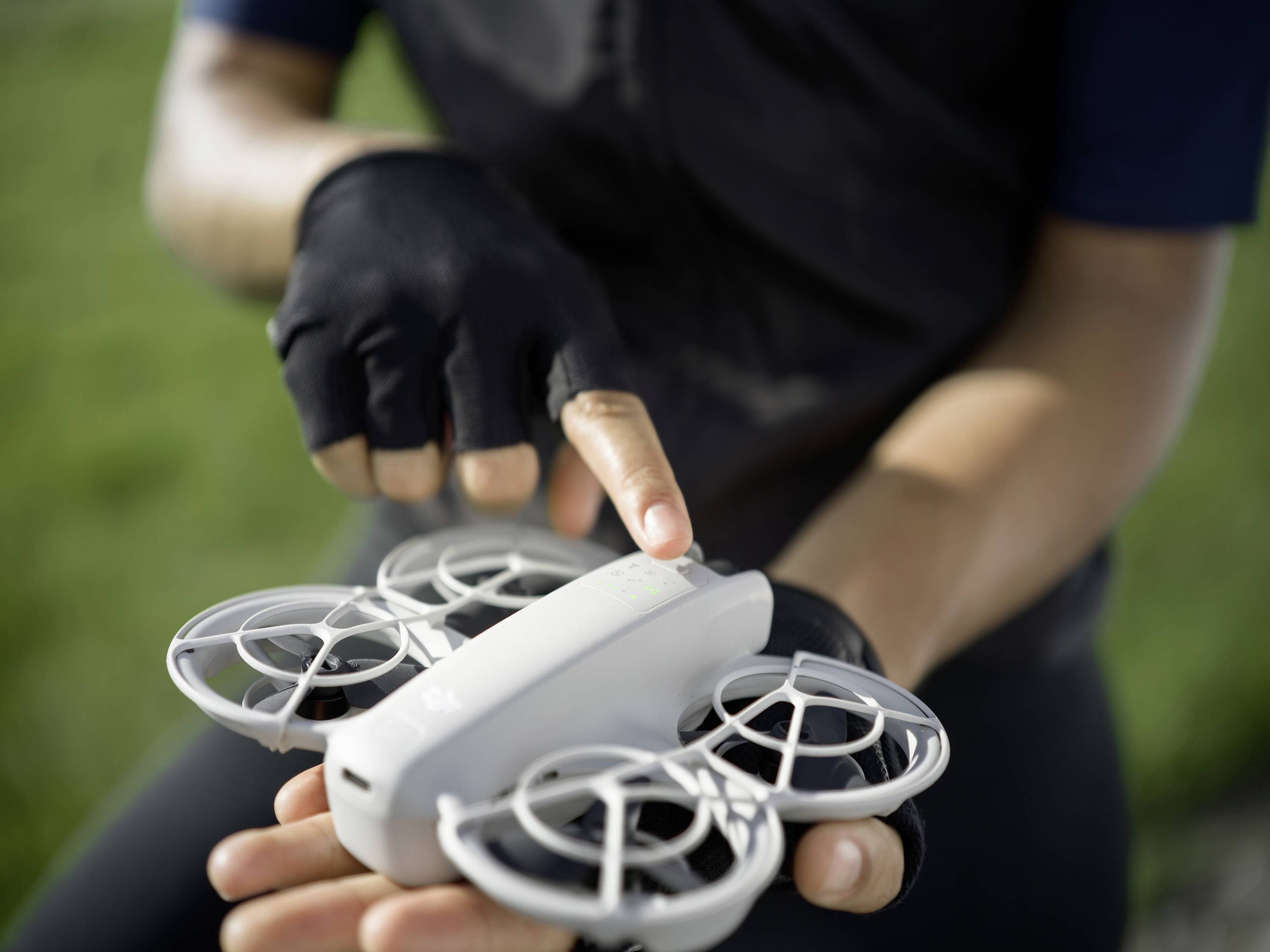 Een persoon houdt een kleine drone in de hand, klaar om op te stijgen. De focus ligt op de drone, terwijl een vinger naar een knop wijst.