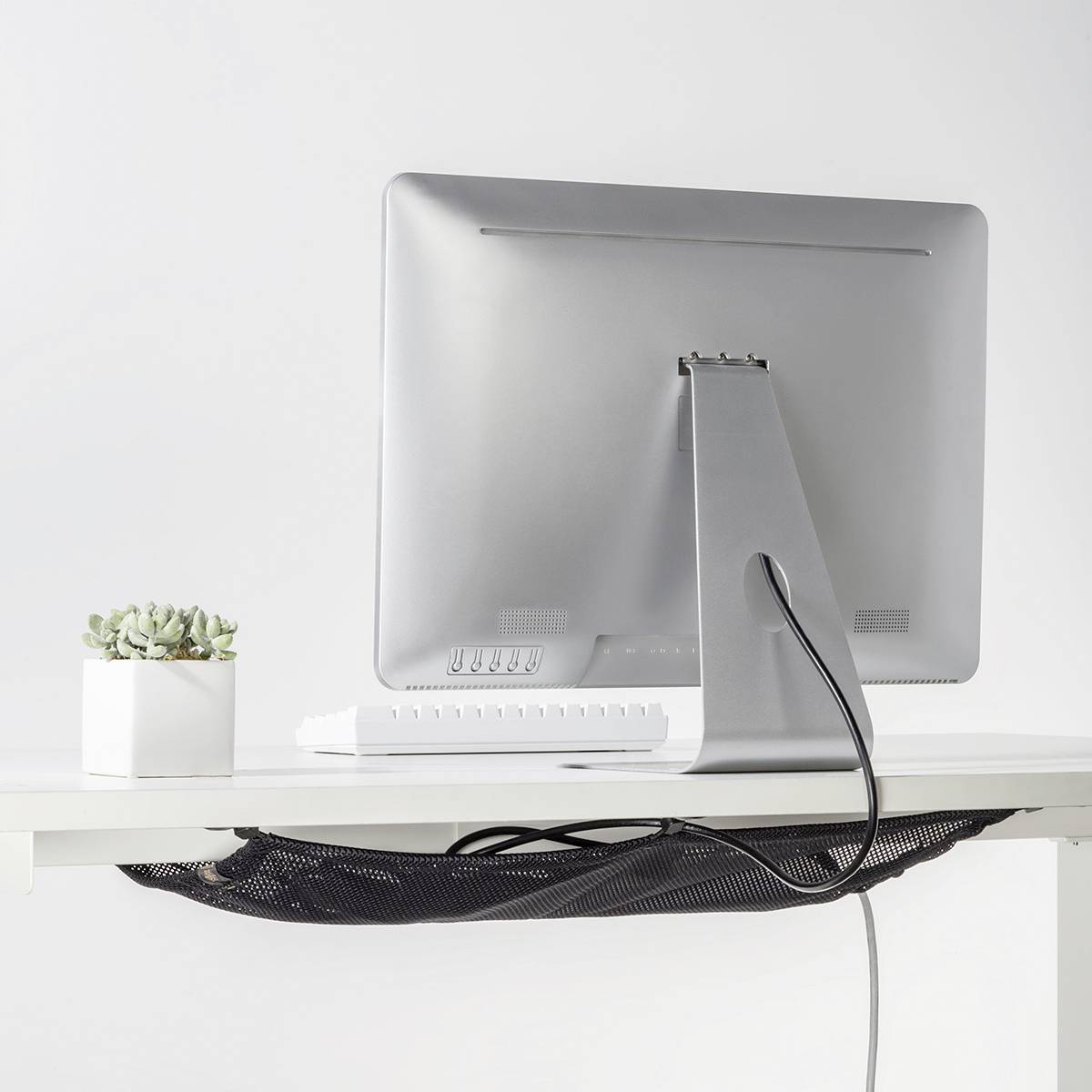 Een monitor op een witte tafel. Ernaast staat een kleine cactus in een witte pot. Kabelbeheersysteem onder de tafel zichtbaar.