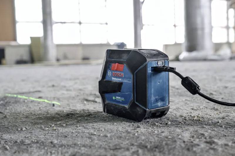 Een Bosch-laserwaterpas op een betonnen vloer projecteert een groene lijn, die de horizontale uitlijning aangeeft in een bouwlocatie-omgeving.