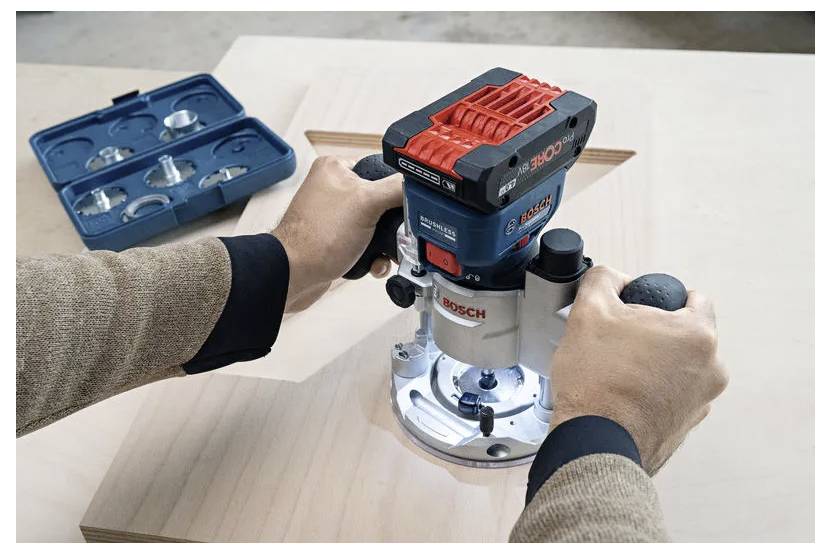 Een persoon gebruikt een Bosch houtfrezen om een ingewikkeld ontwerp uit te frezen op een houten plank, met freesjes tentoongesteld in een kast in de buurt.