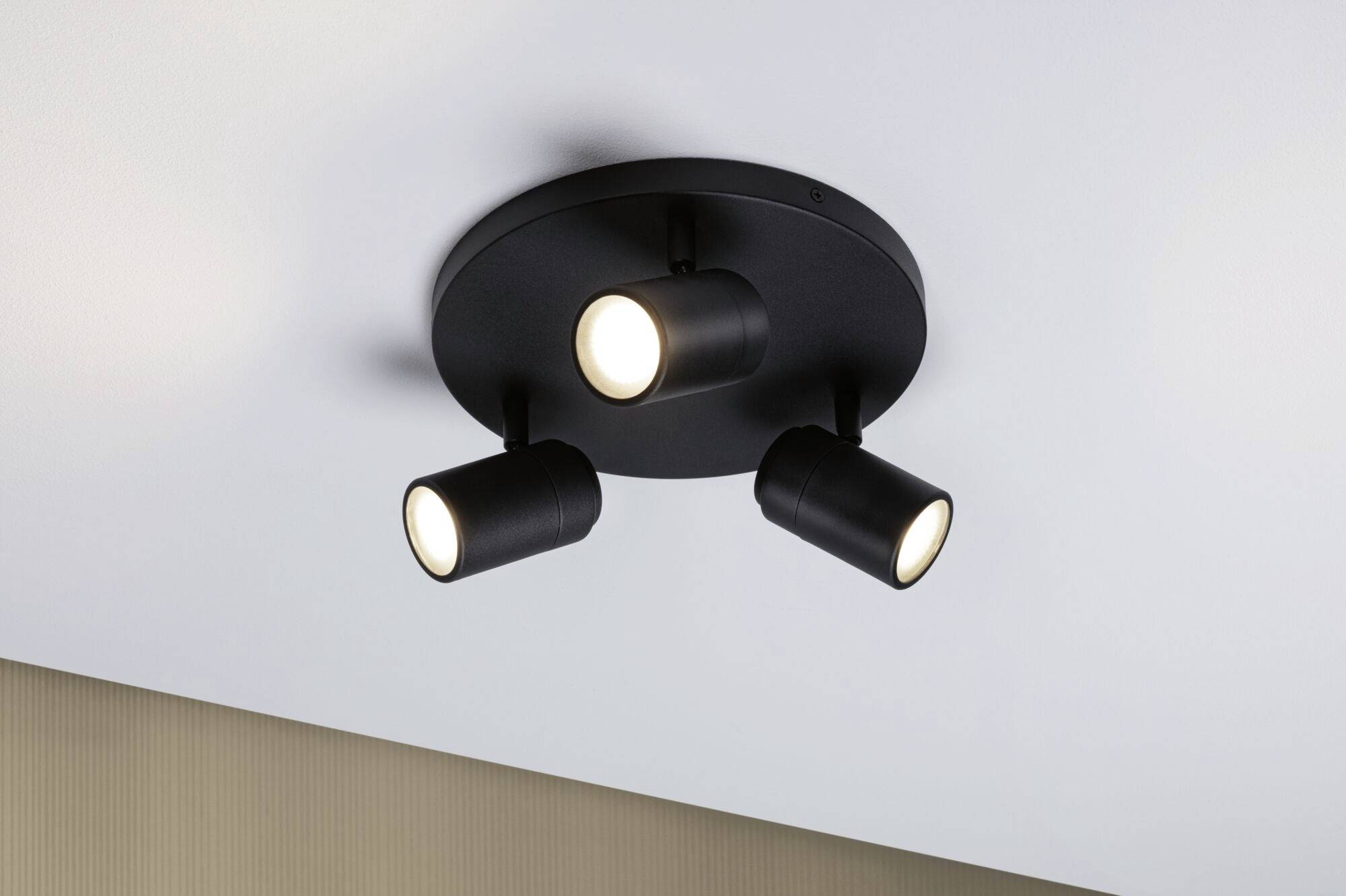 Zwarte, ronde plafondlamp met drie verstelbare spots die aan het plafond is bevestigd.