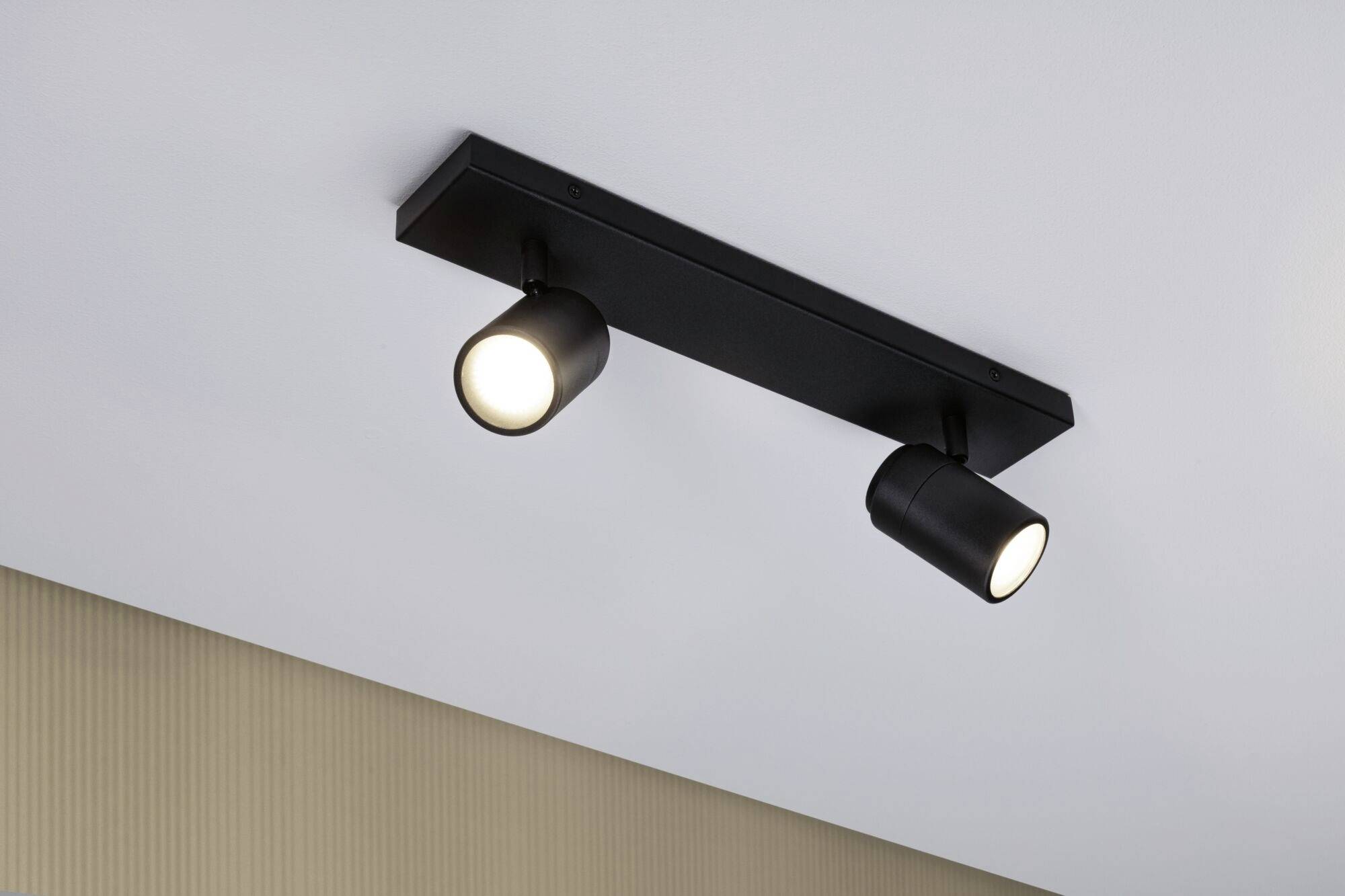 Plafondlamp met twee zwarte, cilindrische lampen die aan een rechthoekige steun zijn bevestigd en naar beneden schijnen.