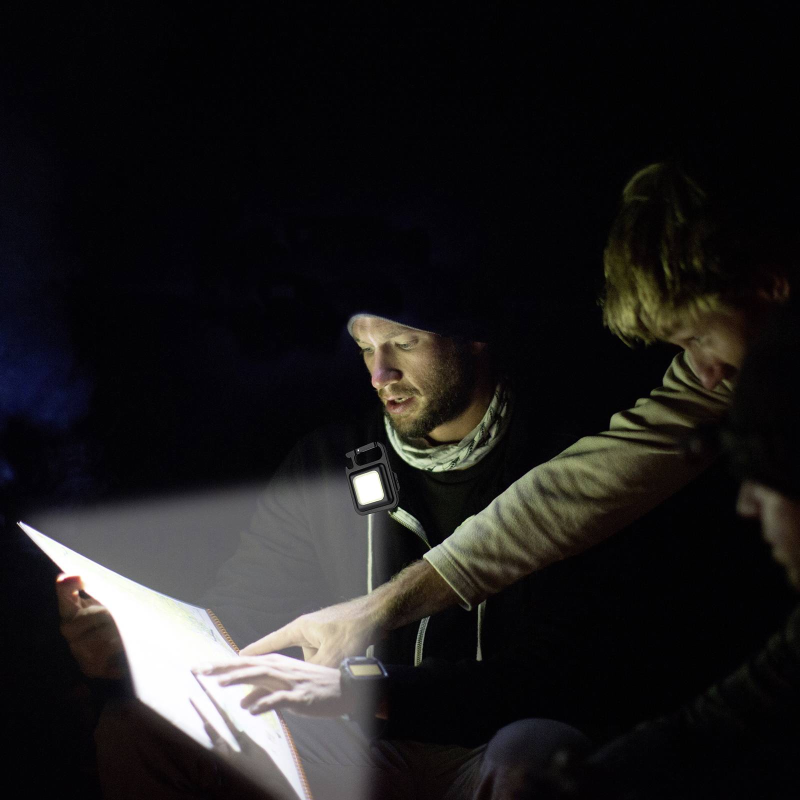 Een groep personen leest een document bij zwak licht. Iemand wijst met zijn hand naar het papier om iets uit te leggen.