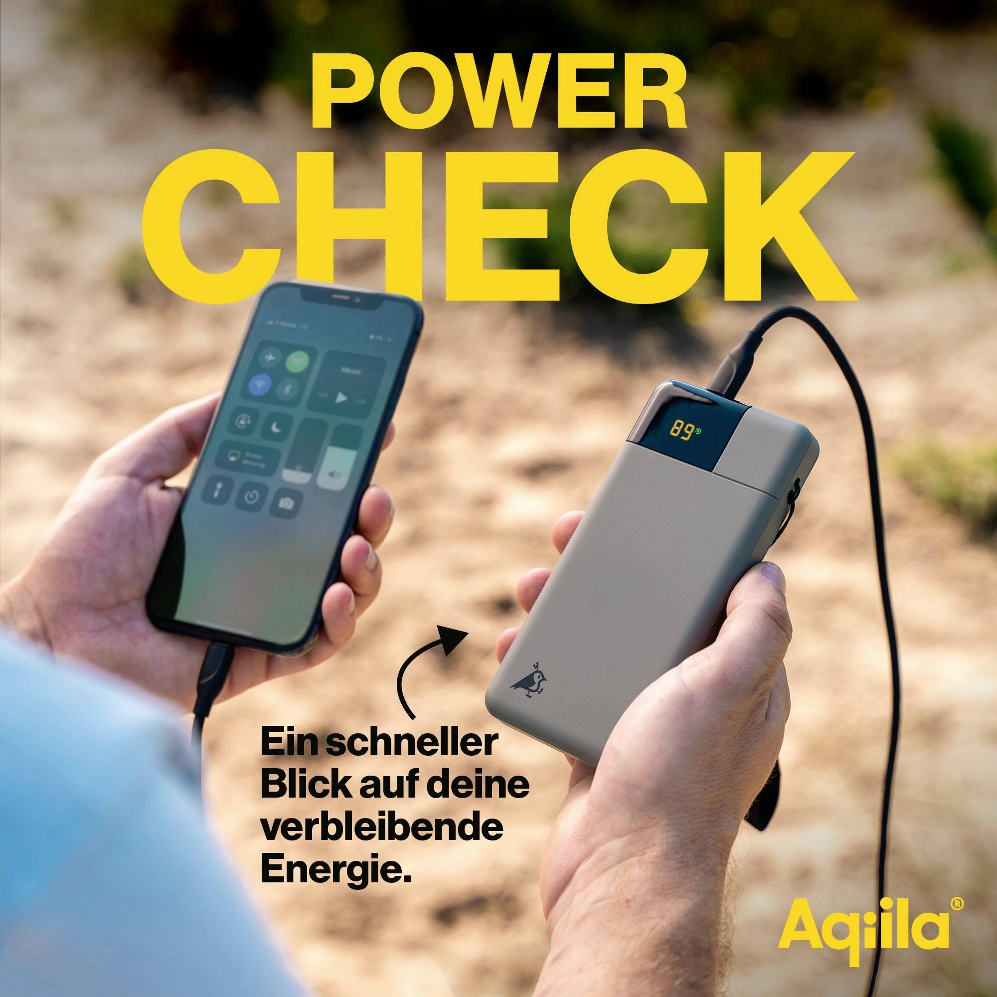 Hand houdt een powerbank met digitaal display vast dat de resterende energie aangeeft. Tweede kabel laadt een smartphone op. Tekst: 'Een snelle blik op je resterende energie.' Merklogo rechtsonder.
