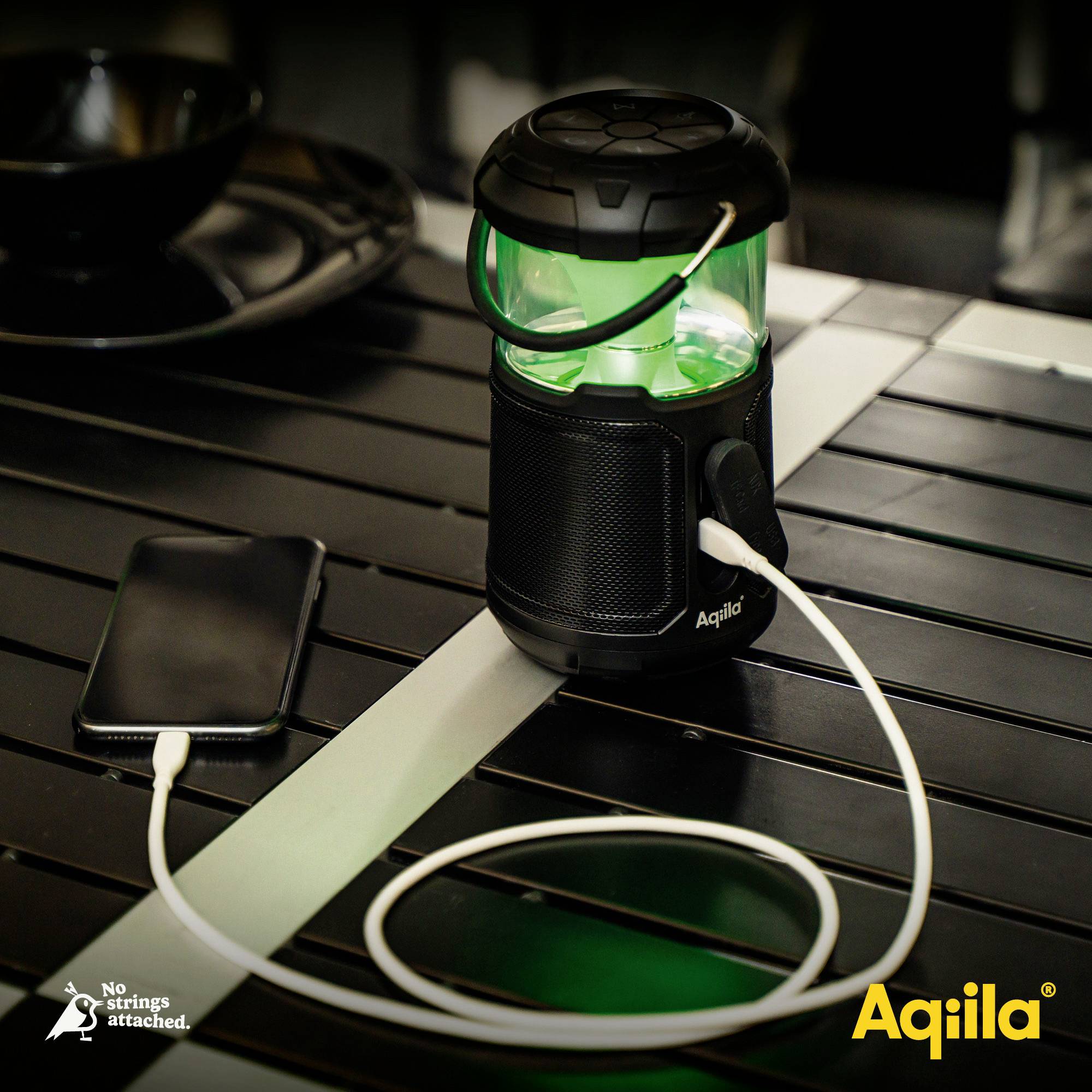 Een draagbare luidspreker met groen oplichtend licht laadt een smartphone op via een kabel. Merknaam 'Aqiila' zichtbaar.